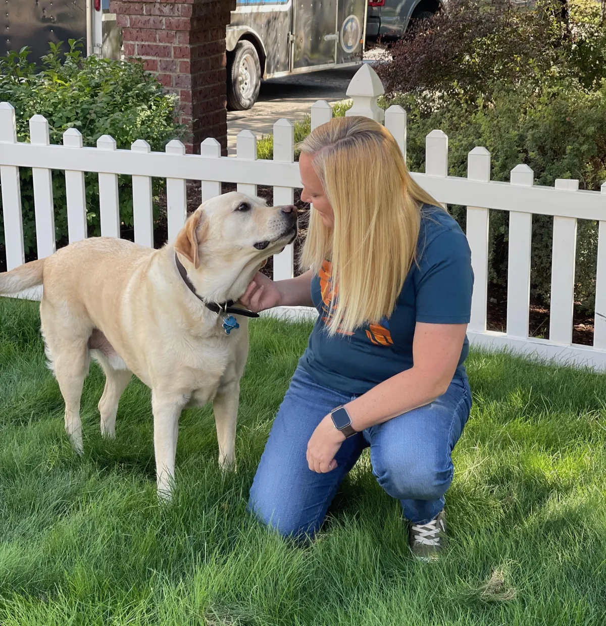 Trainer kneeling with a yellow Labrador in a fenced garden